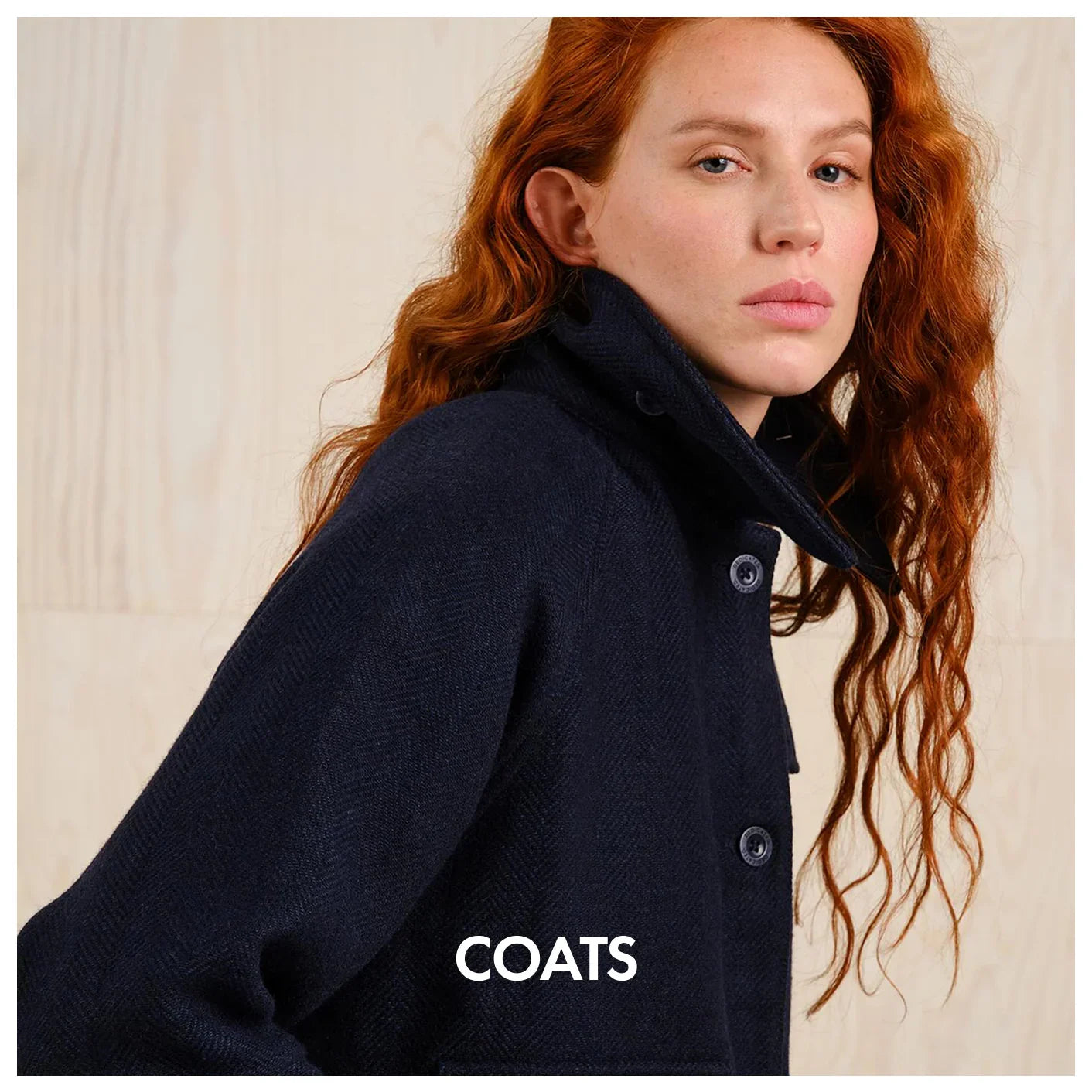 Woman with long red hair wearing a dark navy button-up coat, neutral background, coats collection